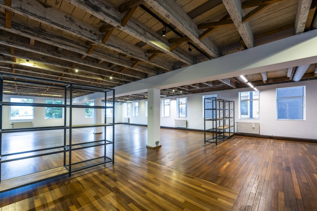 Licht en ruim interieur van een kantoorruimte aan de De Ruijterkade met houten vloer, zichtbare balkenplafonds en metalen stellingen.